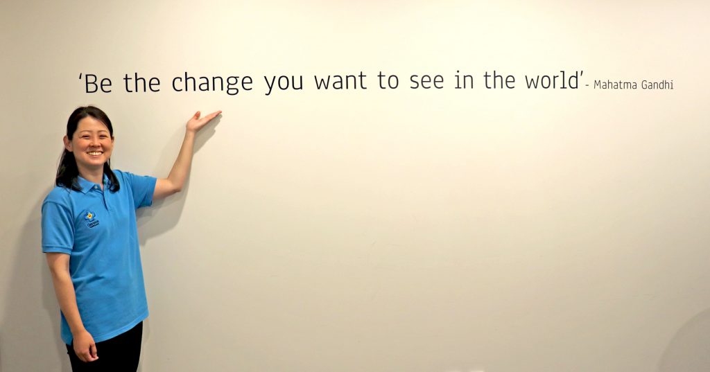 Student posing next to 'Be the change you want to see in the world' quote.