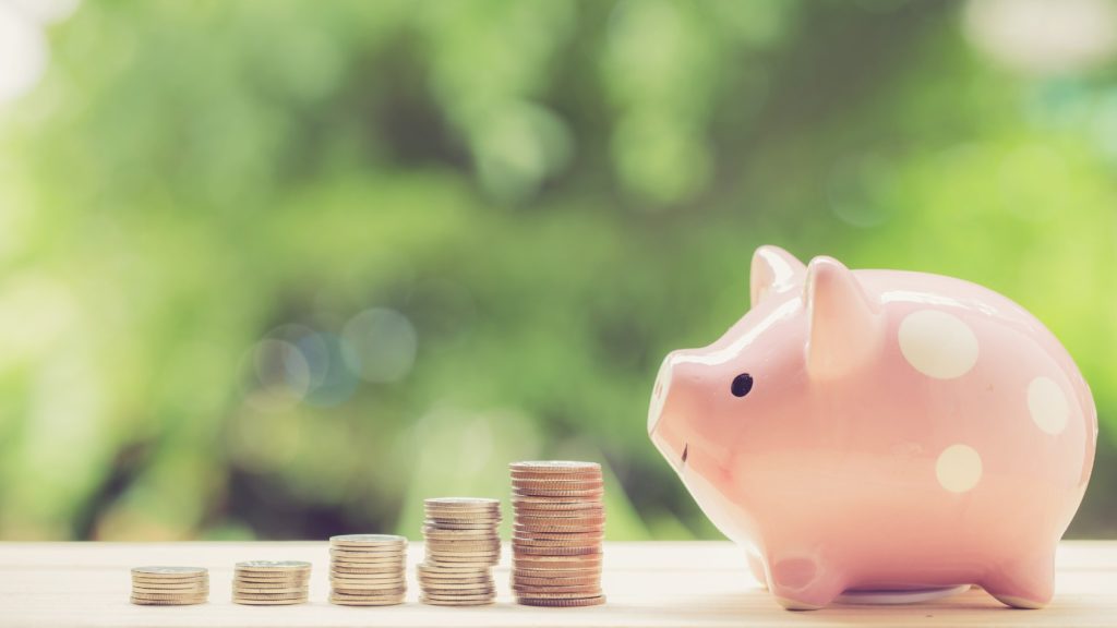 Pink piggy bank next to stacked coins